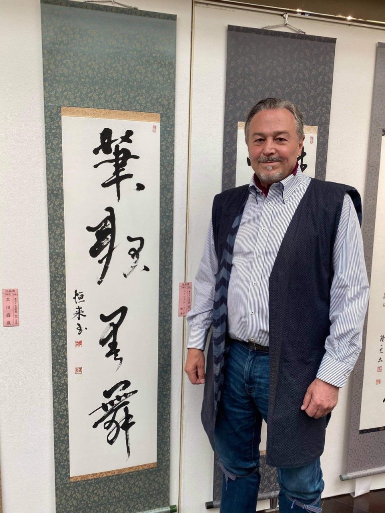 William Reed stands beside his shodo work at a gallery