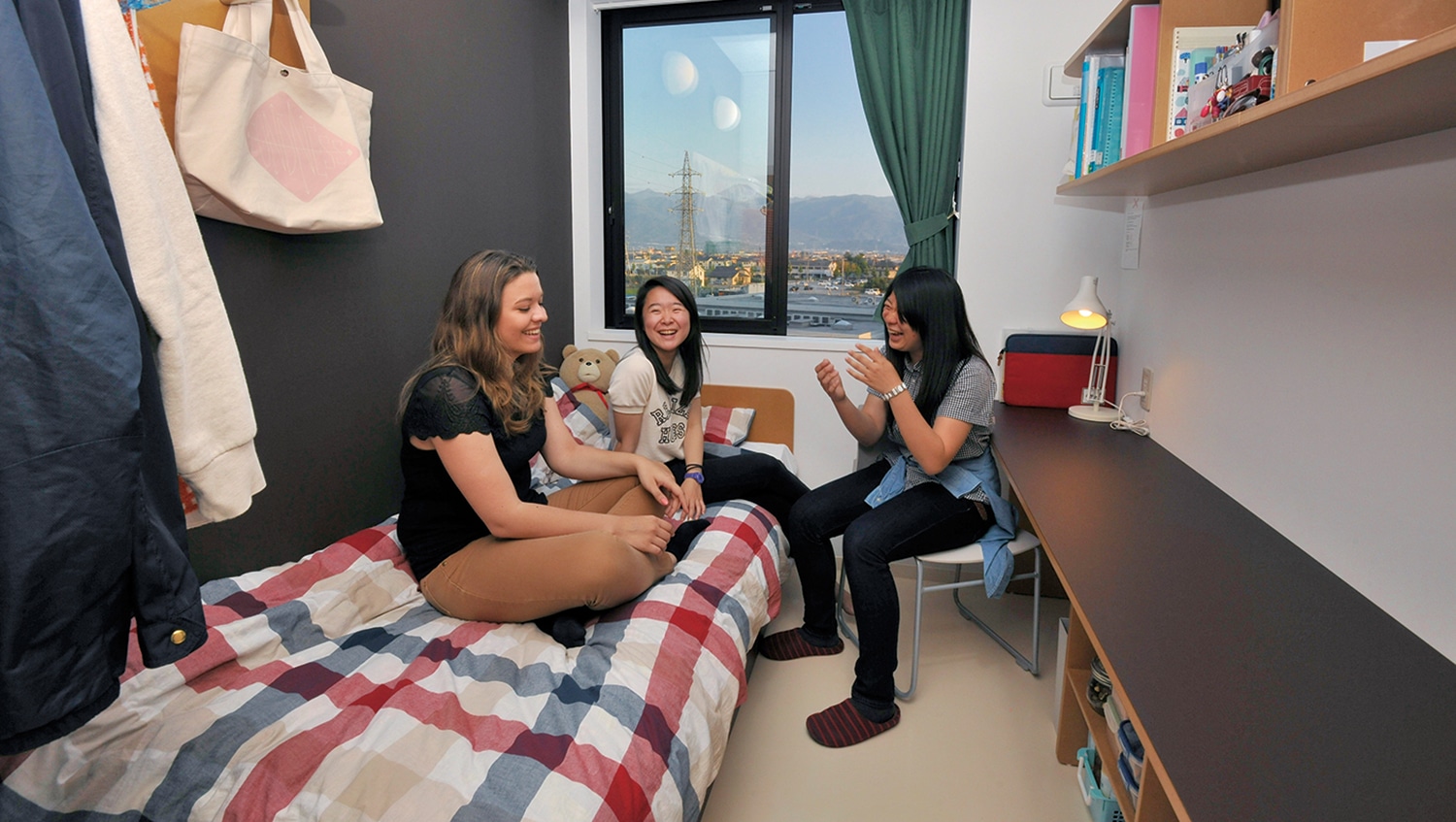 Three female iCLA students chatting in a dorm room