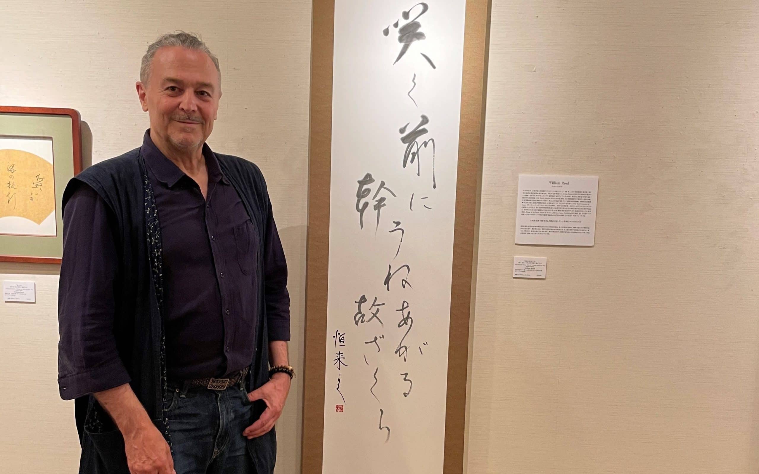 iCLA Professor William Reed stands beside his Japanese Calligraphy artwork 