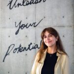 iCLA international student smiles and poses for the camera. Behind her is a wall with the words "Unleash Your Potential".