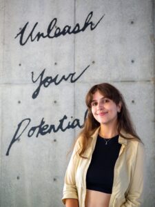 iCLA international student smiles and poses for the camera. Behind her is a wall with the words "Unleash Your Potential".
