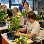 iCLA students sit at desks in a classroom, learning how to do Japanese flower arrangement or ikebana from a master, who is demonstrating how to arrange the flowers.