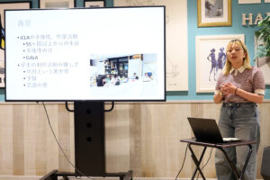 A female iCLA student gives a presentation on her proposal, Diversity Exhibition. Beside her is a screen showing a PowerPoint slide.