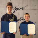 Two smiling iCLA students hold their certificates for the Yamanashi Gakuin University Student Challenge Program, looking proud to be chosen.
