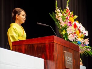 President Takako Aoyama stands at the podium to give a commencement speech to the graduating class of Fall 2025.