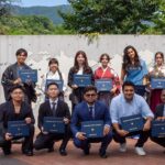 Holding their diplomas, iCLA graduates take a commemorative group photo outside of the International College of Liberal Arts logo.