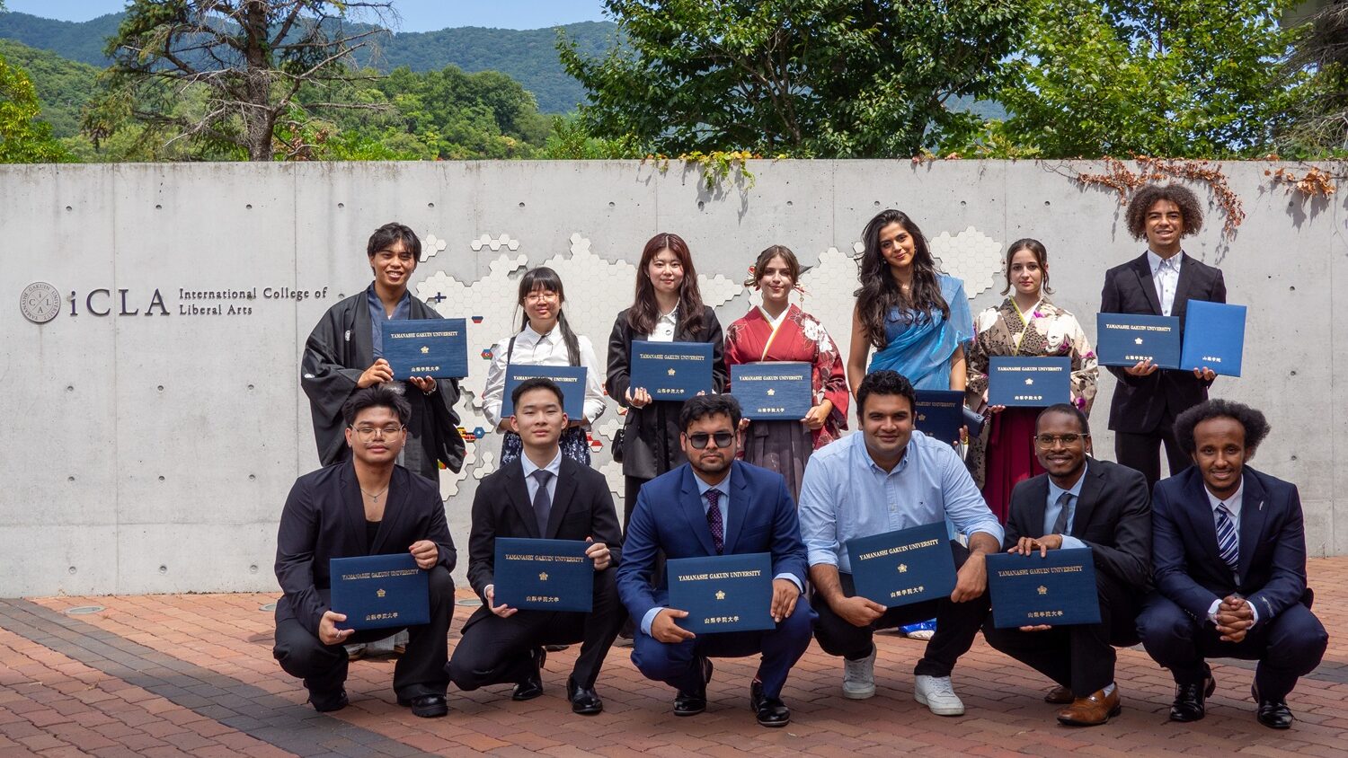 Holding their diplomas, iCLA graduates take a commemorative group photo outside of the International College of Liberal Arts logo after the Fall 2025 Graduation Ceremony.