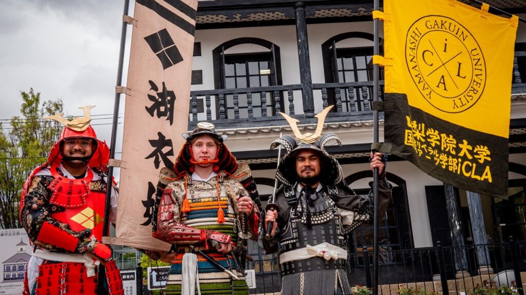 iCLA students joining the Shingenko Festival are wearing samurai armor and proudly holding up a bright yellow iCLA flag and the Princess Koihime Troop banner.