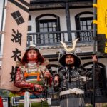 iCLA students joining the Shingenko Festival are wearing samurai armor and proudly holding up a bright yellow iCLA flag and the Princess Koihime Troop banner.